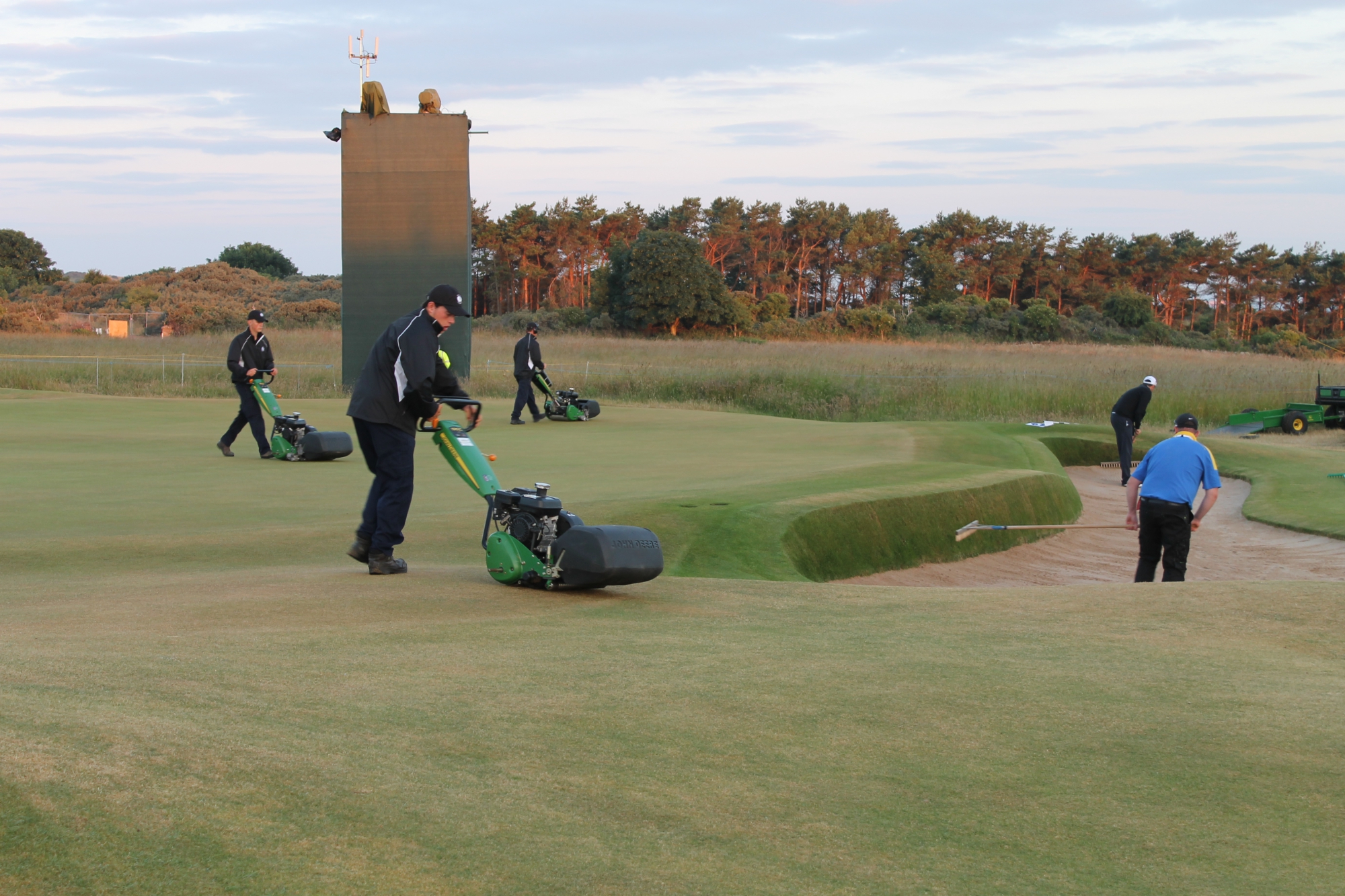 Greenkeepers mowing green and sweeping bunkers
